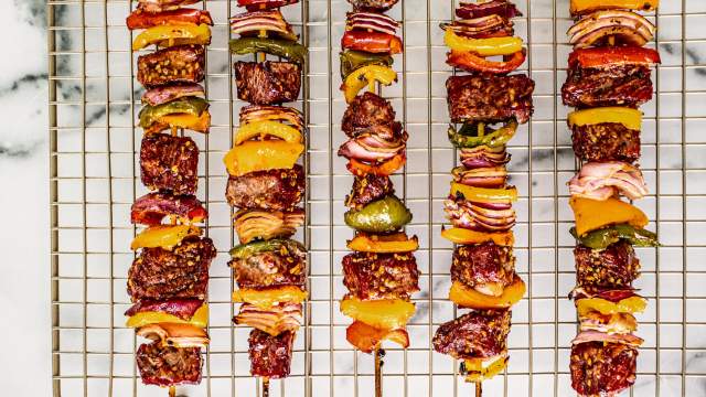 Teriyaki beef kabobs with red onions, bell peppers, and teriyaki sauce on skewers on a rack. 