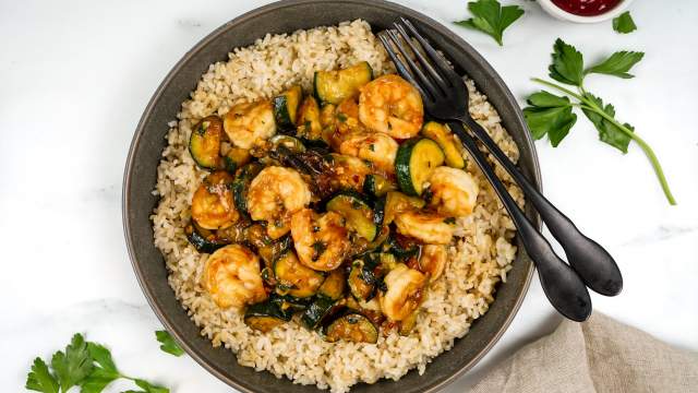 Thia baisl shrimp stir fry with zucchini, cooked shrimp, and brown rice in a bowl. 