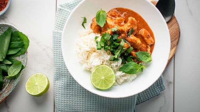 Thai red coconut curry chicken in a bowl with steamed rice, cilantro, basil, and fresh lime.