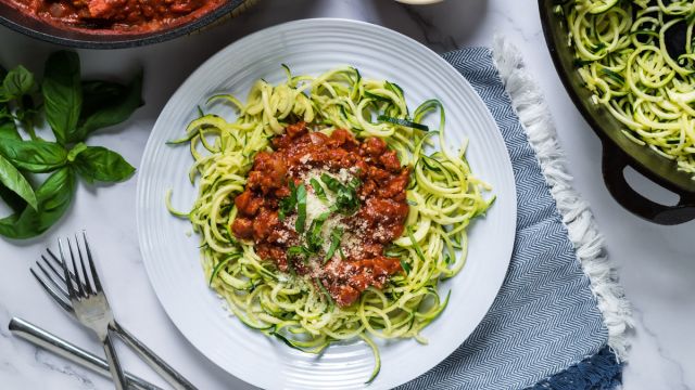 Tomato basil zucchini noodles with ground turkey served on a plate with basil and Parmesan cheese.