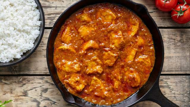 Tomato braised chicken thighs in a skillet with rice and tomatoes.