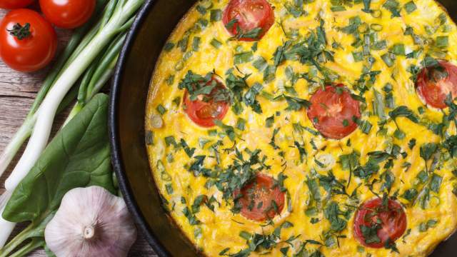 Baked frittata with tomatoes and goat cheese in a skillet with fresh herbs. 