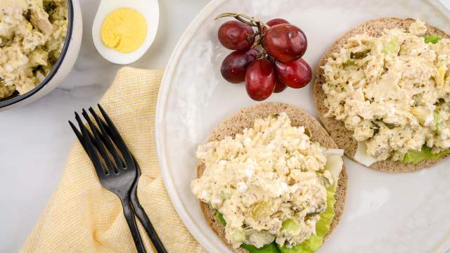 Tuna egg salad on a sandwich thin with red grapes and lettuce.