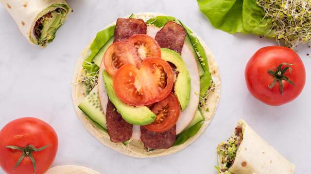 Turkey BLT wraps with deli turkey, cooked bacon, lettuce, tomato, and sprouts on a wrap.