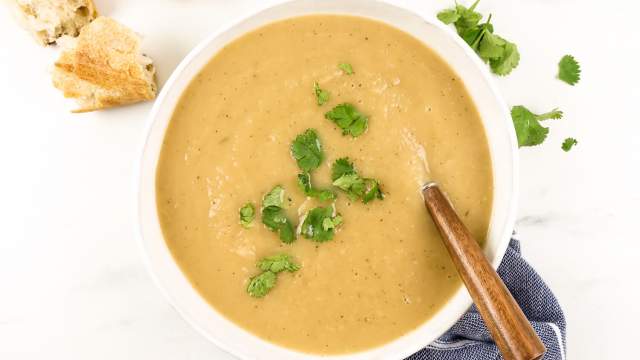 Turnip soup with potatoes in a bowl with fresh herbs, a wooden spoon, and fresh bread.