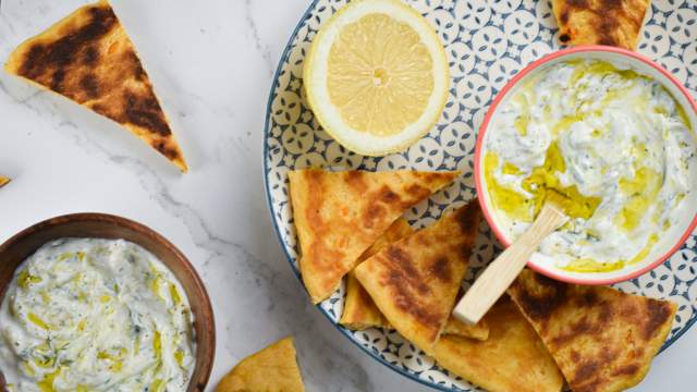 Tzatziki made with Greek yogurt, cucumbers, lemon, garlic, and dill in a bowl with pita wedges on the side.