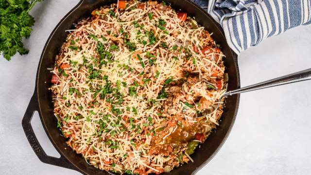 Unstuffed pepper skillet with ground beef, turkey sausage, quinoa, and bel peppers in a cast iron skillet topped with Parmesan cheese.