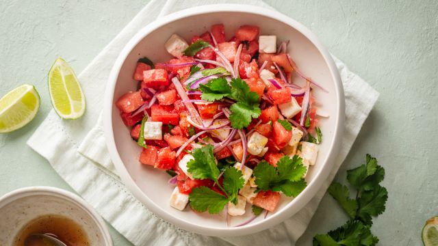 Watermelon and feta salad with cilantro and served with lime vinaigrette in a white bowl with fresh limes on the side.