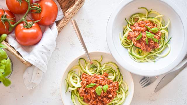 Zucchini noodle bolognese with zucchni noodles, turkey bolognese sauce, and basil on a plate with tomatoes on the side.