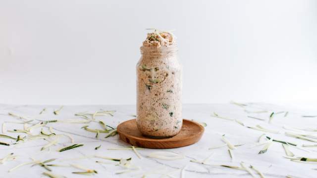 Zucchini bread overnight oatmeal in a glass jar with cinnamon, rolled oats, almond butter, and shredded zucchini.